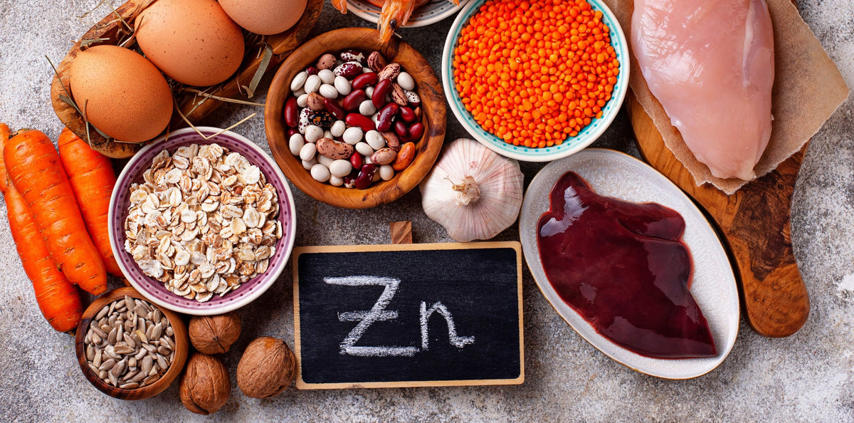 Zinkreiche Lebensmittel liegen auf einer weißen Tischplatte verteilt. Zwischen den Lebensmitteln liegt eine Tafel mit der Aufschrift