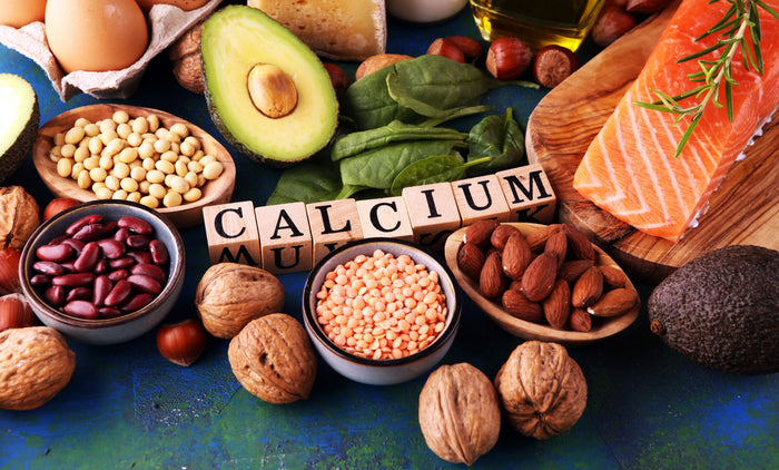 Calciumreiche Lebensmittel liegen auf einem Tisch. In der Mitte  ist das Wort Calcium mit Holzwürfeln ausgelegt .