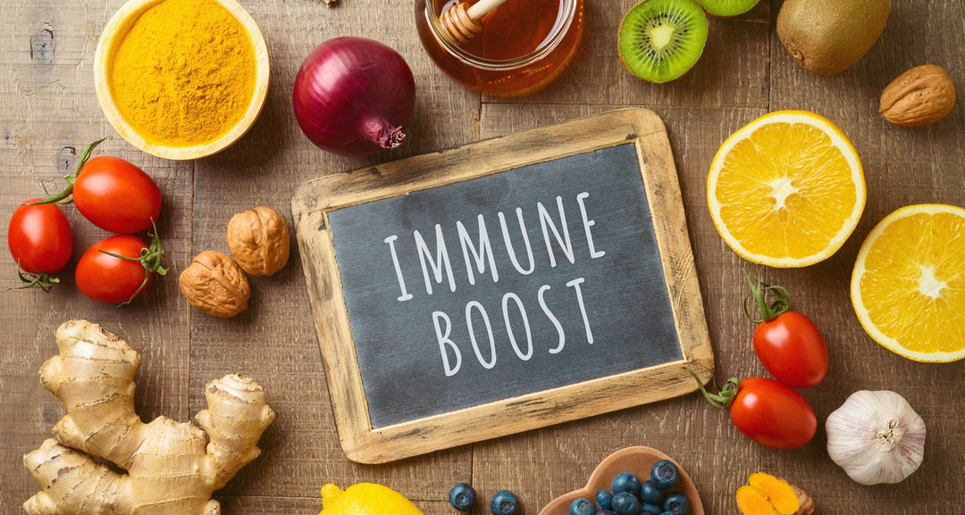 Verschiedene Lebensmittel wie Nüsse, Tomaten, Zwiebeln und Ingwer liegen auf einem Holztisch. In der Mitte liegt eine Tafel mit der Aufschrift "Immunsystem stärken".
