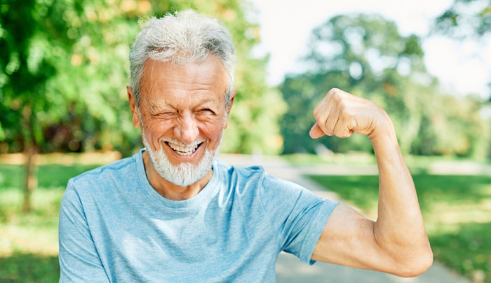 Ein älterer Mann steht in einem Park und spannt seinen Bizeps an.