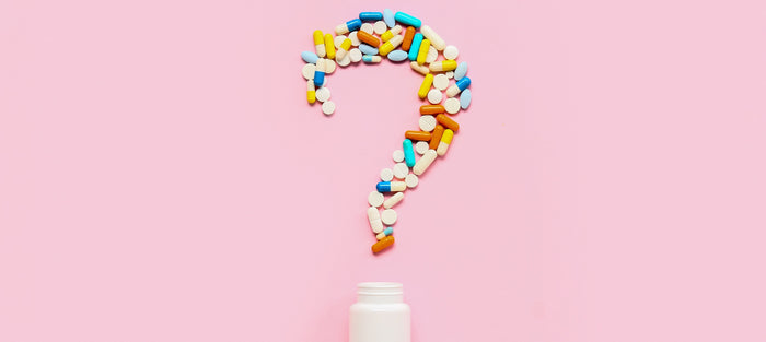 Eine Fragezeichen aus Nahrungsergänzungsmittelkapseln  liegt auf einem pinken Hintergrund.