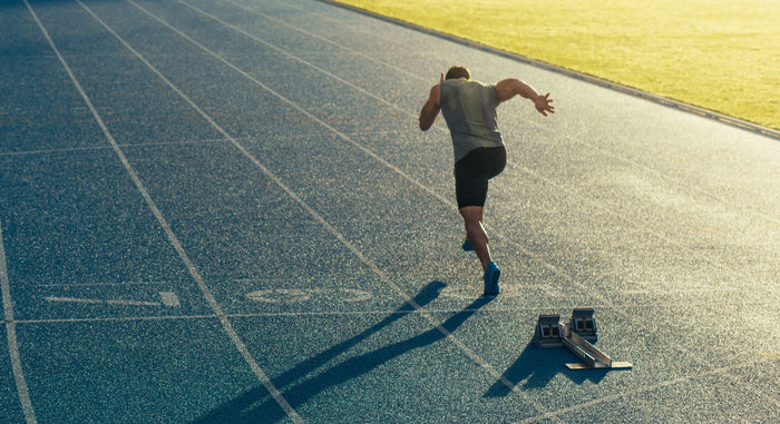 Ein Läufer startet einen Sprint von einem Block auf einem Sportplatz.