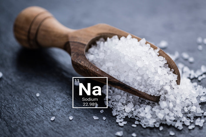 Natrium salz liegt auf einem Holzlöffel. Der Löffel liegt auf einer steineren Tischplatte.