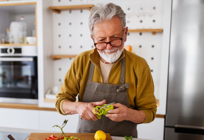 Ein älterer Herr steht in der Küche und präpariert eine Mahlzeit. 