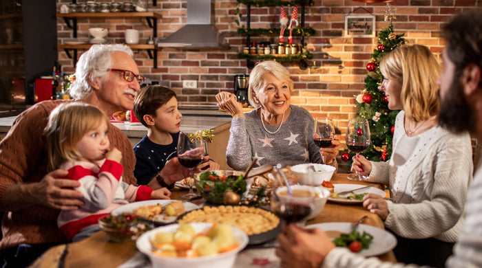 Eine Familie bestehend aus Eltern, Großeltern und Kindern sitzt an einem Tisch und isst zu Weihnachten Abendbrot.